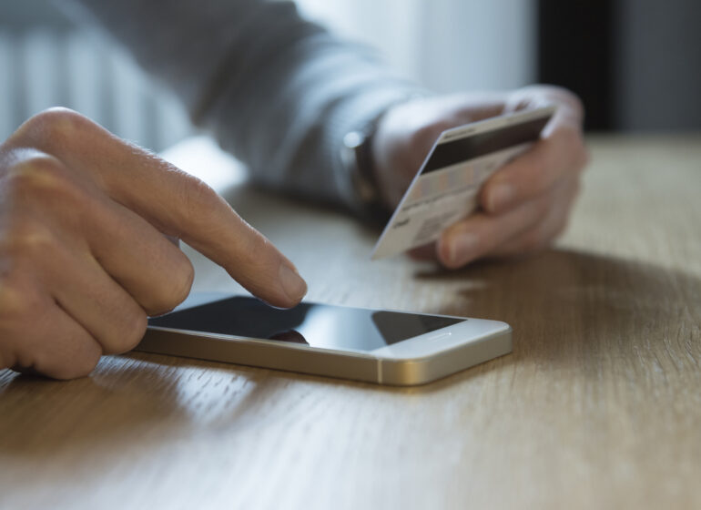 Eine Person hält eine Kreditkarte in der Hand und tippt auf einem Handy, das vor ihr liegt.