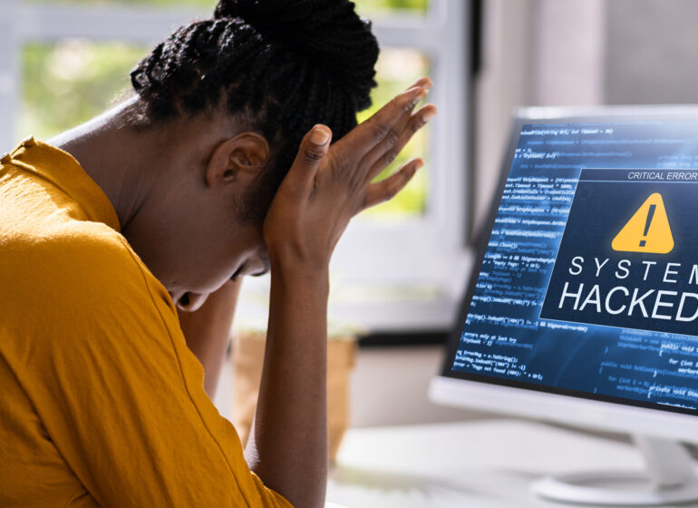 Eine Frau sitz vor dem Computer. Auf dem Monitor ist der Hinweis "System Hacked" zu sehen - Hackerangriff